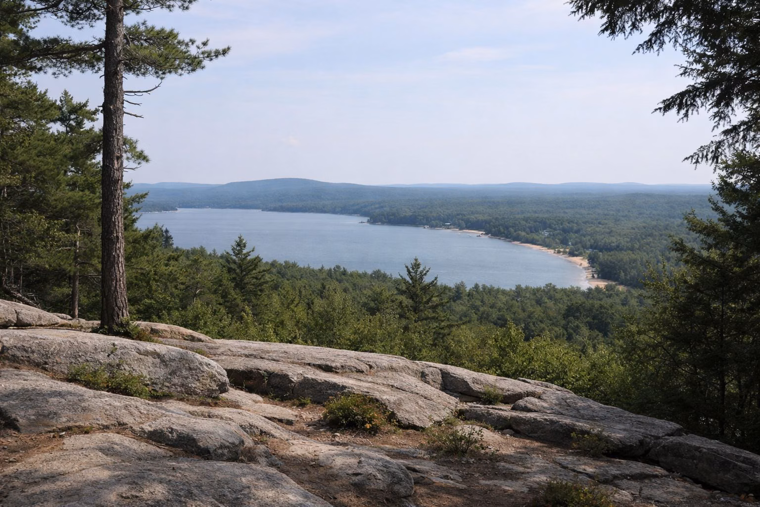A wooded hilltop with low ledges and a view across forest to distant lakes