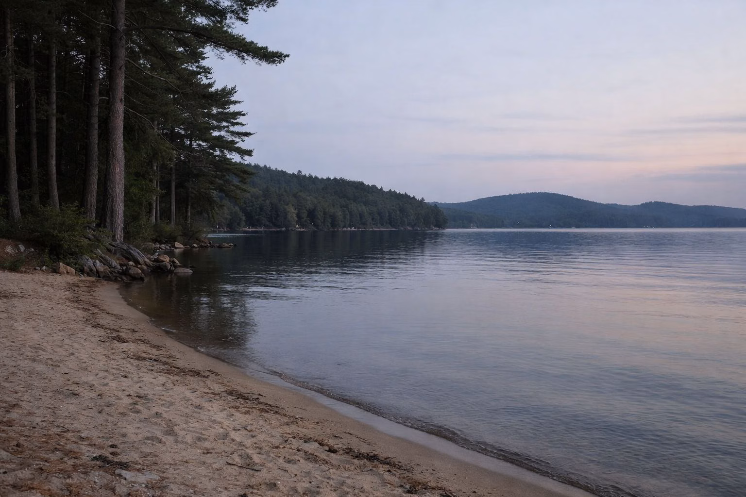 A quiet empty lake shoreline with pines and smooth water at dusk